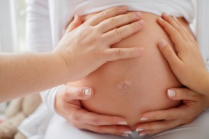 Several hands touch the belly of a pregnant woman. She hugs her