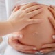 Several hands touch the belly of a pregnant woman. She hugs her